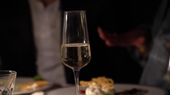 A Glass of Champagne on the Table in the Evening Against the Background of a Couple in Love