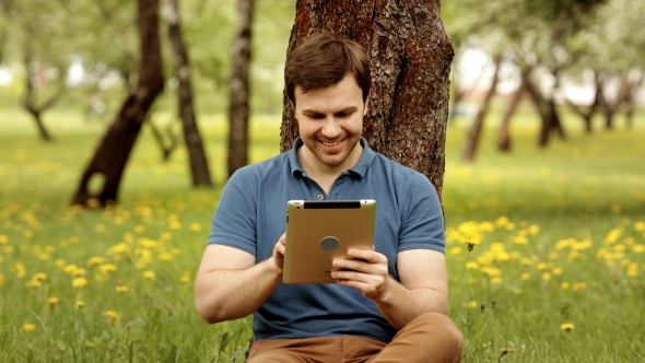 Handsome Smiling Hipster Man Using His Tablet Pc On a Sunny Day