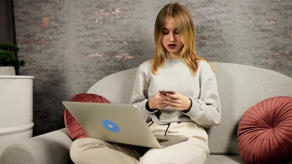 Dolly in Young Woman Using Mobile Phone While Holding Laptop on Lap Sitting on Sofa During alt