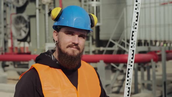 Portrait of a Modern Worker with a Beard in a Hard Hat and Headphones.