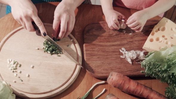 Mother And Daughter Cutting Onion And Garlic On Wooden Board alt