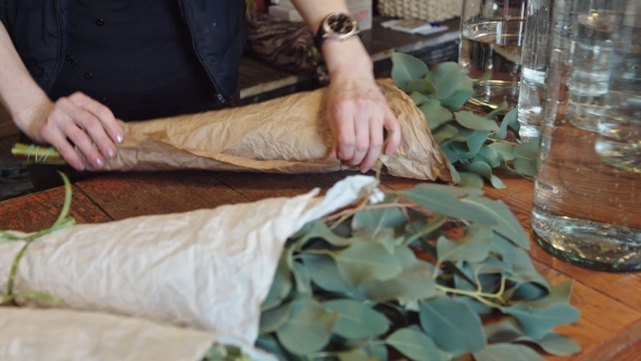 Woman Florist Wraps Something In a Sheet Of Parchment And Bandaging Tape alt