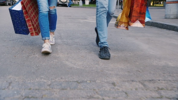 Man And Woman Are On The Sidewalk With Shopping Bags In The Picture Can Be Seen Only The Legs alt