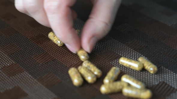 Woman's Hand Counts Capsules Pills On The Table
