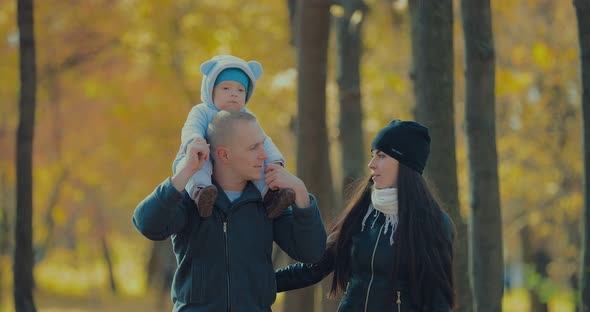Happy Father Carrying His Smiling Son Next To Mother in the Autumn Park alt