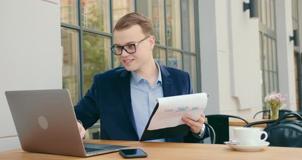 A Businessman is Looking Through Documents and Working on a Laptop alt