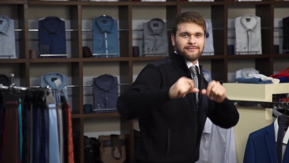 Young Attractive Man With a Beard, Dressed In a Business Suit, Dancing In a Men's Clothing Store. alt