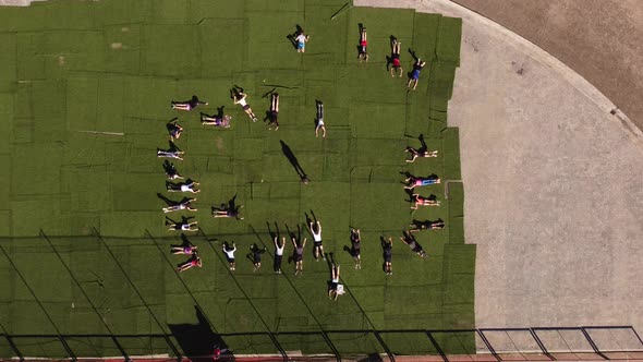 Group of kids lying on green carpet outdoors during physical education class. Aerial drone directly alt