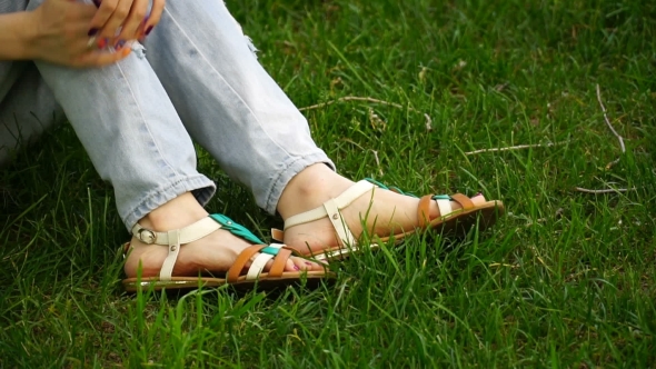 Caucasian Young Woman Sitting On The Grass In The Park Buttons Their Sandals. Footage Girl Relaxing alt