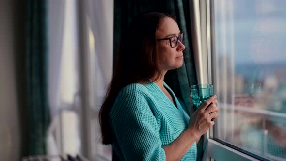 A Happy Woman in the Morning in a Bathrobe is Standing at the Window of Her Apartment Rejoicing in a alt