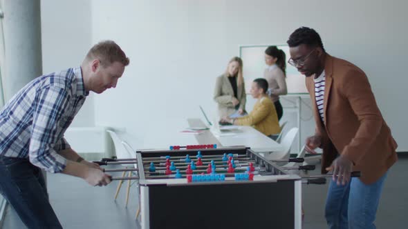 Young handsome casual multiethnic business people playing table football and relaxing at office