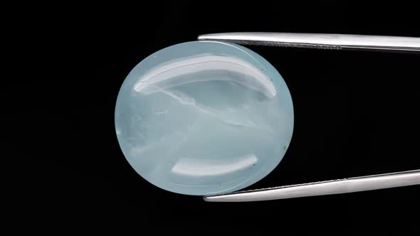 Natural Oval Cabochon Aquamarine in the Tweezers on Black Background