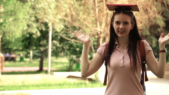 Footage Young Beautiful Woman Walking In The Park. Girl Put The Tablet On His Head. alt