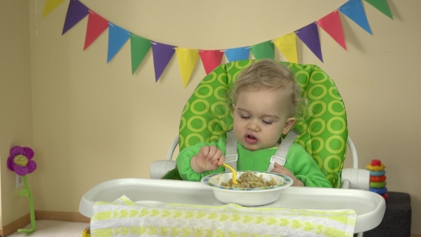 One Year Old Baby Eating Porridge With Messy Face.