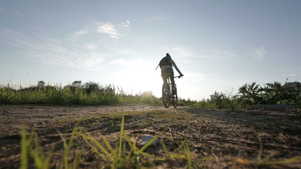 A Young Woman Is Cycling Into The Sunset In The Park