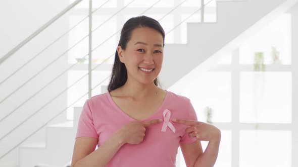 Happy asian woman in pink tshirt showing pink ribbon at home alt