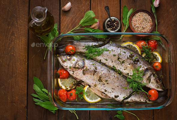 Two baked seabass in a baking dish with spices on an wooden background. Top view