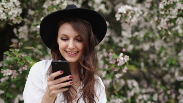 Woman Standing On The Meadow At The Blooming Tree , Using Smartphone alt