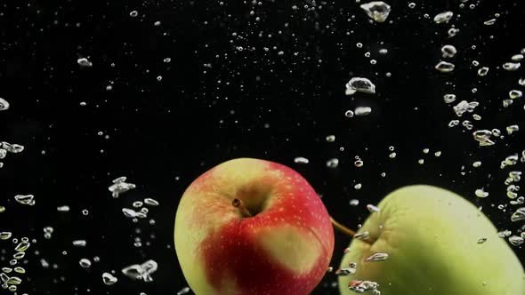 Red and Green Apples Dropping in Splash of Water Isolated on Black Background alt