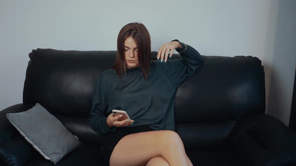 The Thoughtful Young Woman Sits on the Couch Waits for News Picks Up the Receiver and Then Raises alt