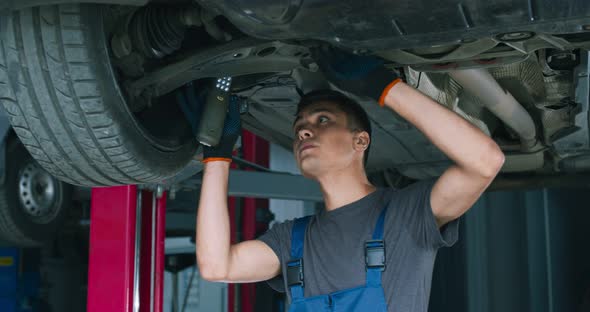 Young Male Mechanic Repairing Car Suspension, Standing Under Vehicle at Garage alt