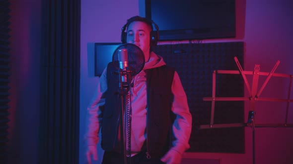 A Man in Headphones Wearing a Hoodie Rapping Through the Pop-filter in the Microphone - Recording alt