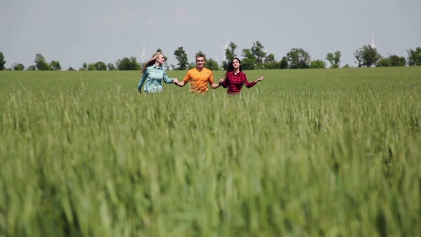 Three Friends. A Man And Two Girls Holding Hands Running On The Green Field.
