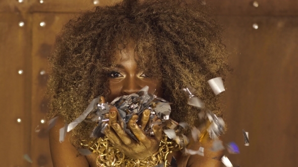 Portrait Of Sexy African American Female Model With Gold Glossy Makeup Blows Silver Confetti