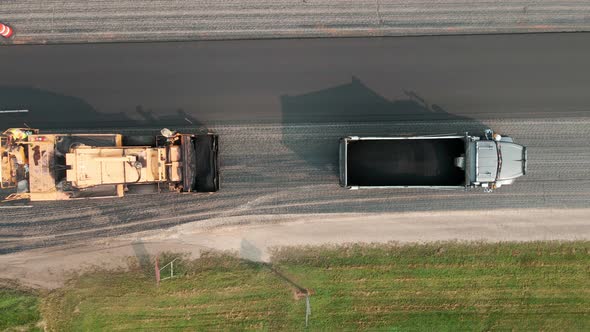 Birds eye view of blacktop paver crew working to repave rural highway on a summer day.