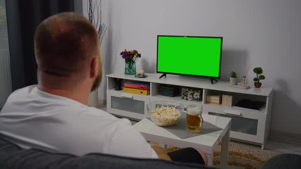 Man Watching Green Screen TV at home. Drink Beer Eating Popcorn. alt