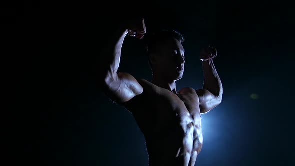 Asian Muscular Man Shows Demonstrates Muscles. Black Background. Slow Motion . Silhouette alt