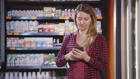 Adult Woman Standing in Supermarket and Using Modern Smartphone