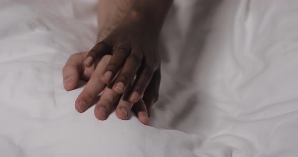 Multi-ethnic Couple in Love Holding Hands While Lying in Bed Together alt