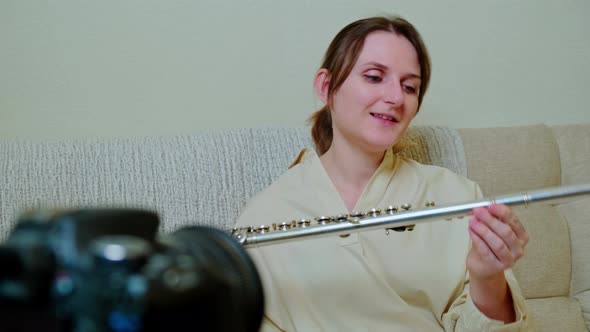 Woman musician with flute looking at video camera at home on sofa in living room