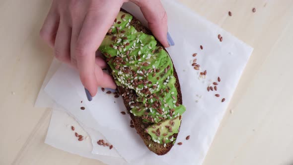 Female hand taking Healthy avocado toast on wooden board. Sesame and flax seeds. Vegetarian food. alt