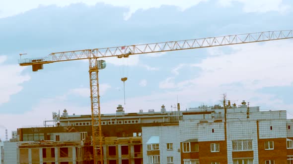 High cranes on a construction site with a house, against the background of the evening sky with suns