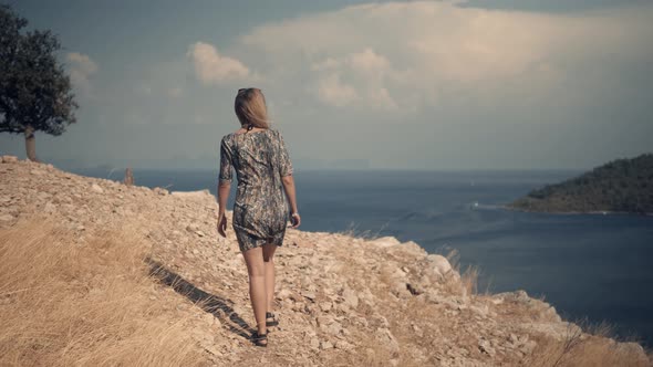 Woman Walking On Sea Cliff.Girl In Dress Walks Under A Rock On Mediterranean Region alt