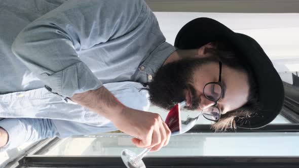 Pleased Bearded Man Drinking Red Wine and Admiring View Form Window at Home alt