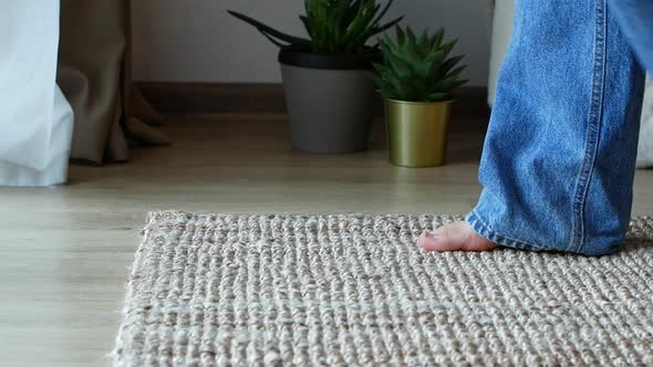 Barefoot woman in jeans comes into the frame standing on a wicker mat