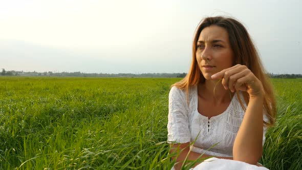 Cute Girl Sitting on the Green Grass and Dreaming. Beautiful Woman Enjoying Nature in Summer Evening alt