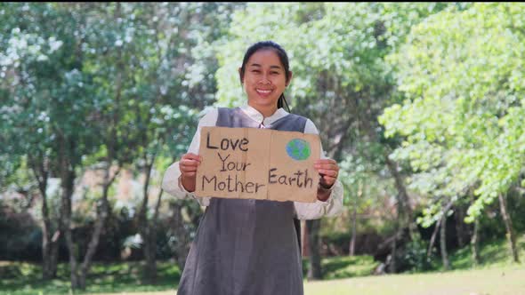 Portrait of woman standing with Love Your Mother Earth poster at the summer park. alt
