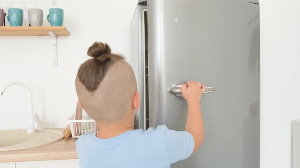 Teenage Boy Opens the Refrigerator in the Kitchen alt