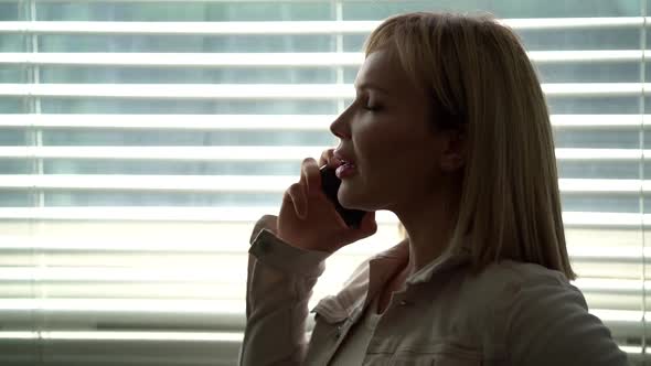 Young Blonde Woman Is Talking By Mobile Phone and Gossiping with Friend or Colleague alt