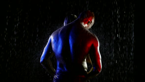 a Couple with Golden Metallic Skin Embraces in Streams of Water on a Black Background alt