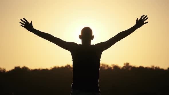 Silhouette of Young Man Raising Hands To Sides and Up Against Sunset Slow Motion alt