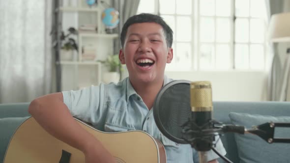 Happy Asian Boy With Guitar And Microphone. The Child Is Broadcasting Live On The Internet alt