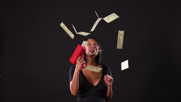 Mixed ethnicity woman shooting money out of a money gun. alt