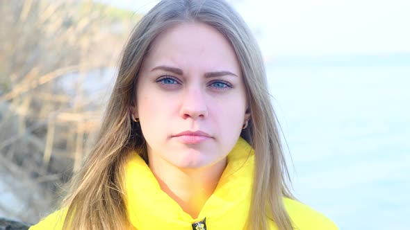 Portrait of a Sad Serious Young Woman Against the Background of the River in a Yellow Jacket on a