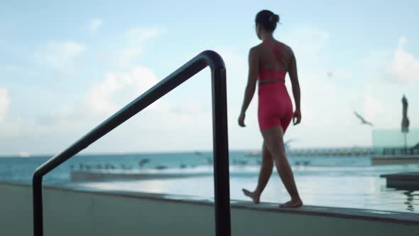 Young Woman Walk Near Swimming Pool on the Sunset in Pink Suit