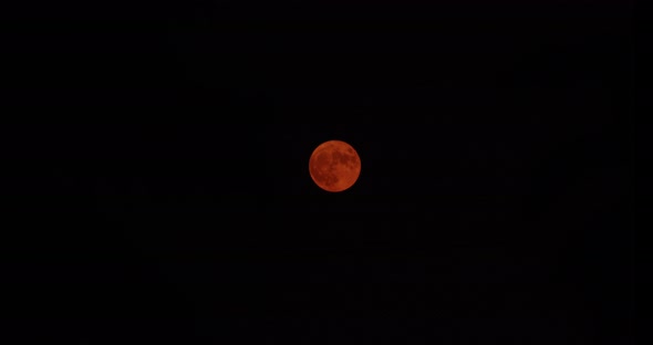 Time-lapse wide shot of a Harvest Moon as it slowly rises from the center the upper left. The color alt